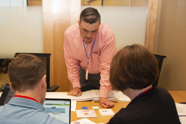 Curbell employee stands at table while describing several different plastic samples to two customers