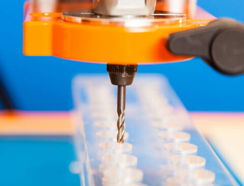 Orange drill drilling holes in plastic sheet on a blue background